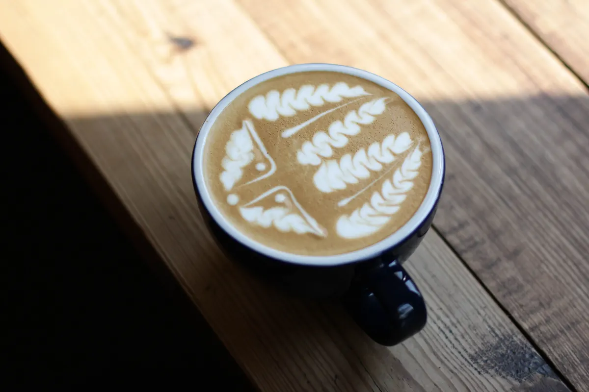Secangkir latte dengan latte art berbentuk daun di atas meja kayu