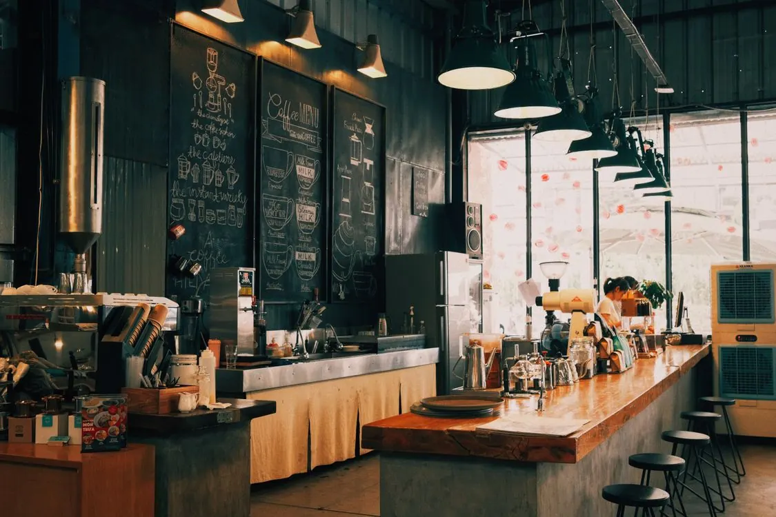 Suasana interior kedai kopi dengan bar panjang, papan menu kapur, dan lampu gantung