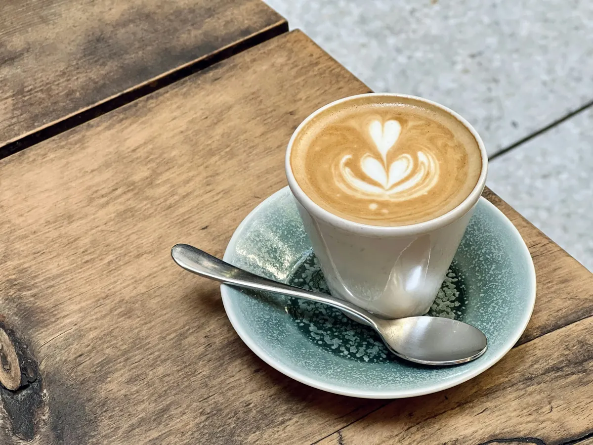 Latte dengan latte art hati dalam cangkir putih di atas talenan kayu